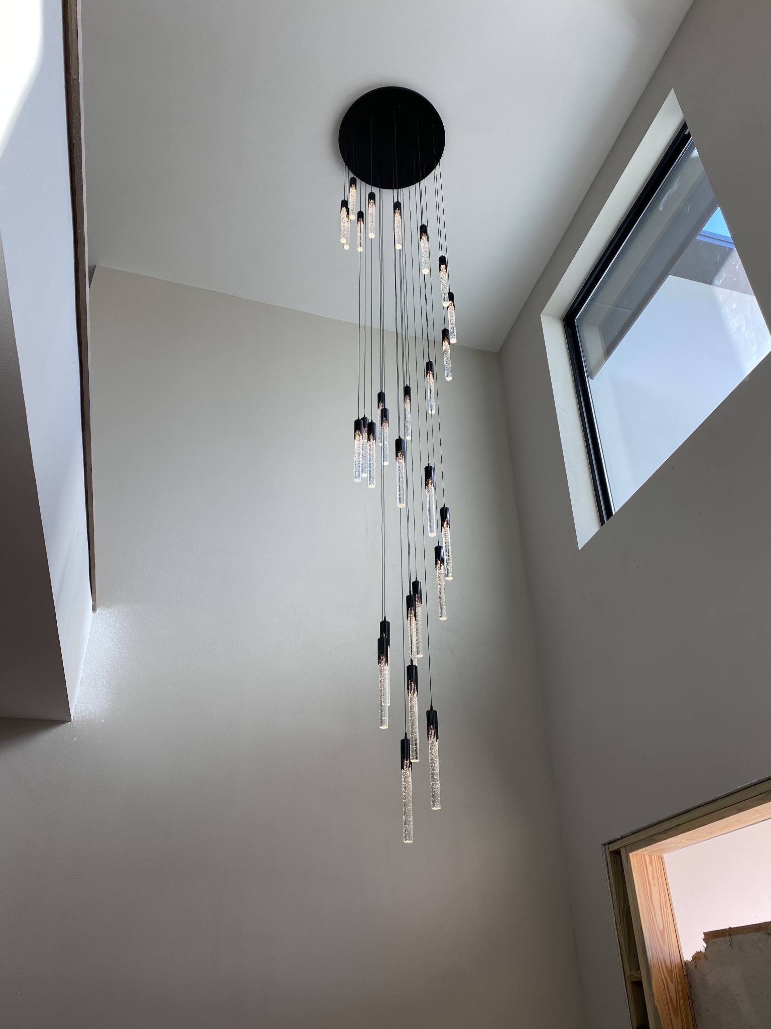Cascading multi-pendant LED chandelier with slim glass tubes suspended in a tall two-story entryway.