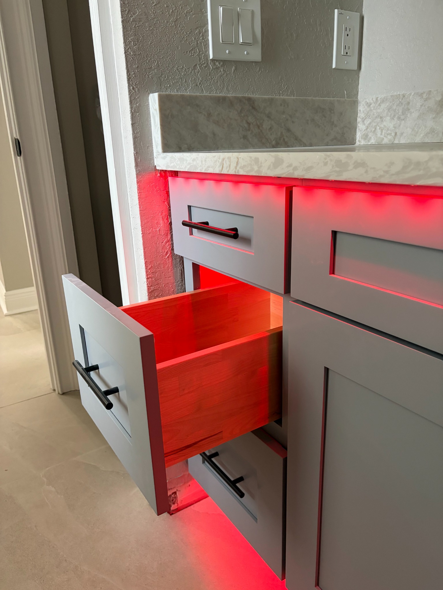 Close view of a bathroom vanity drawer pulled open, showing red LED accent lighting spilling from beneath the cabinet and countertop.