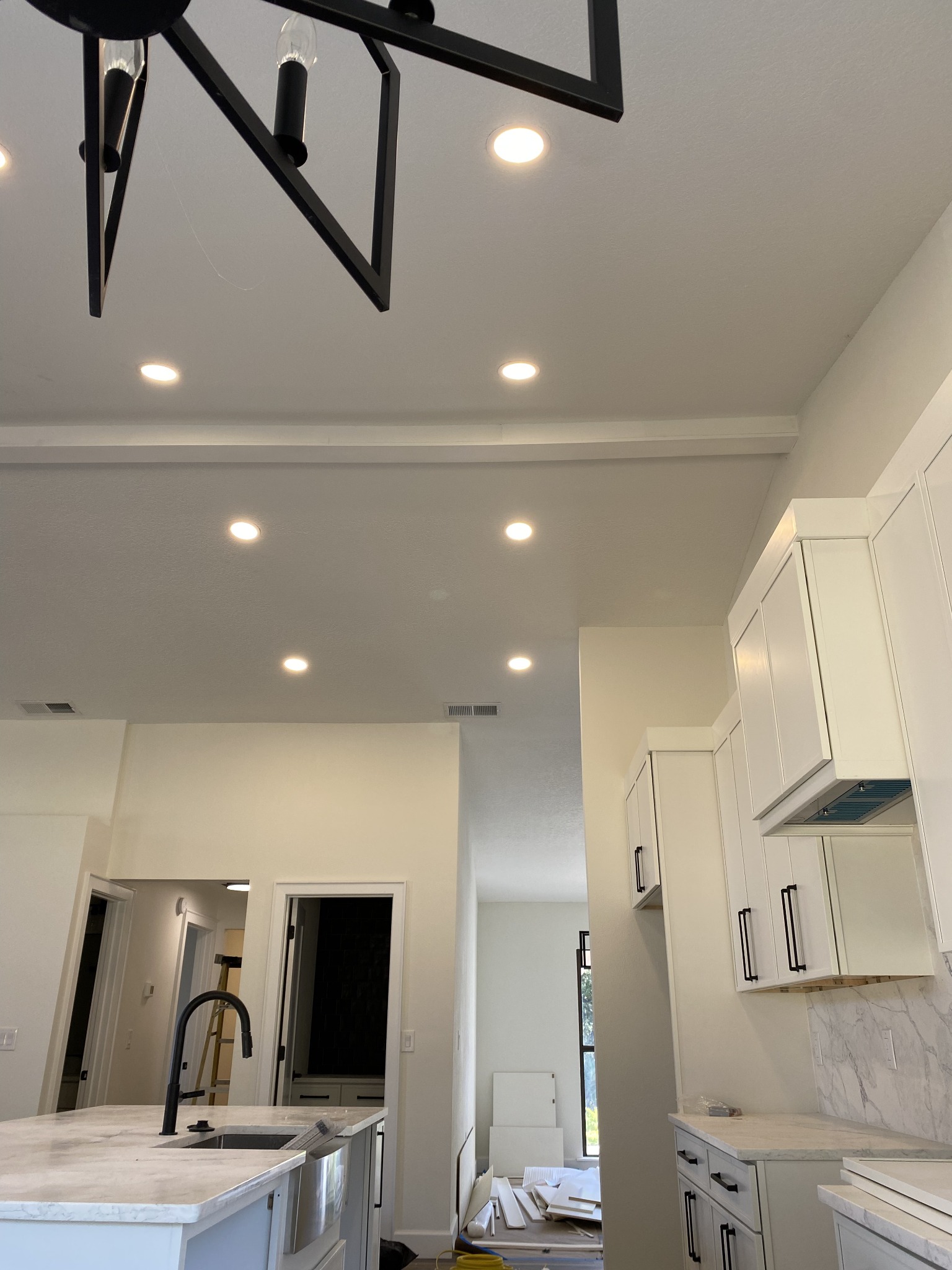 Kitchen ceiling with recessed LED downlights laid out around a black geometric pendant fixture hanging over the sink.