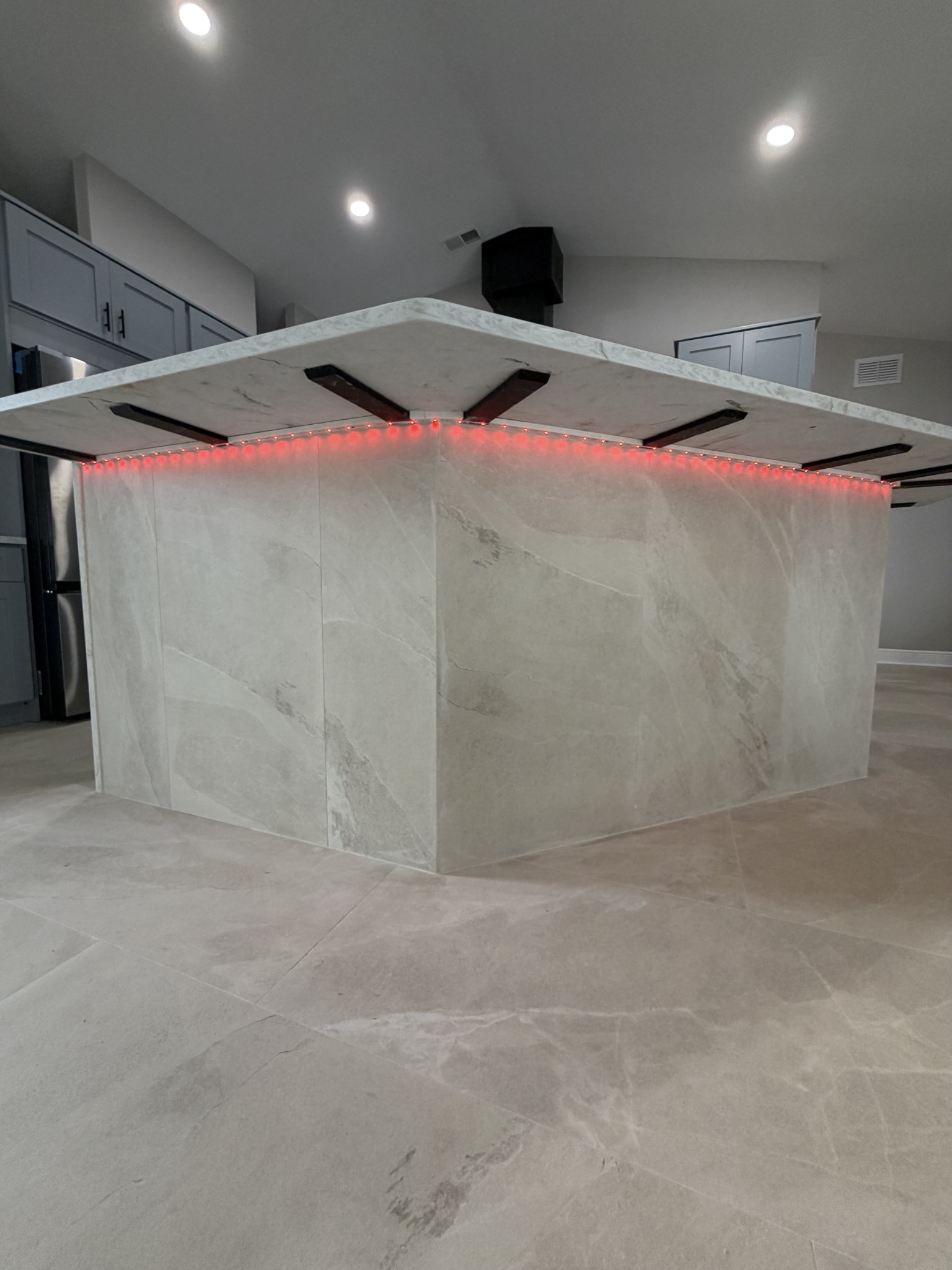 Wide view of a kitchen island glowing with red under-counter LED strip lighting beneath a dark wood support frame.