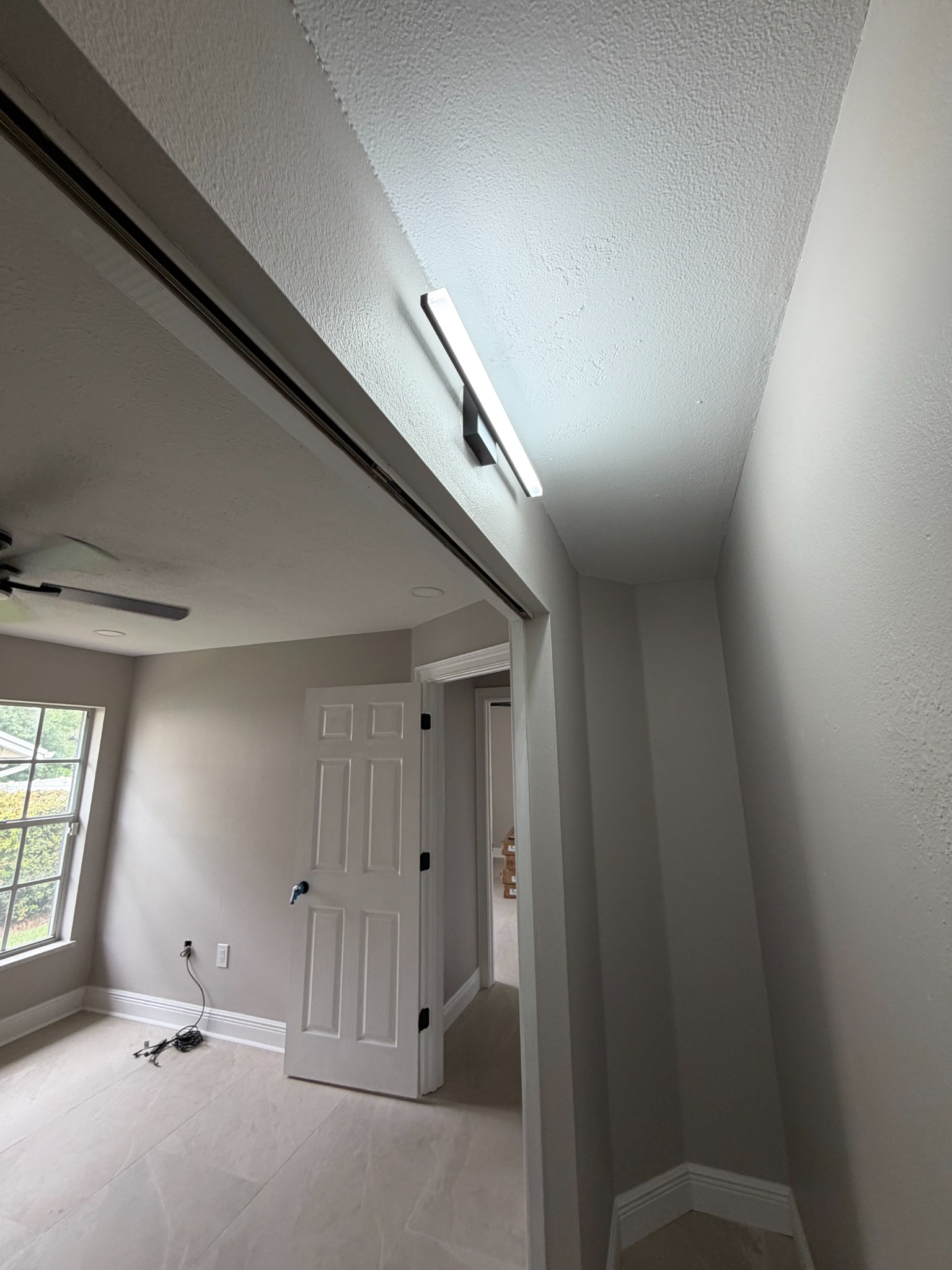 Modern linear LED wall fixture mounted above a doorway opening in a freshly painted hallway.