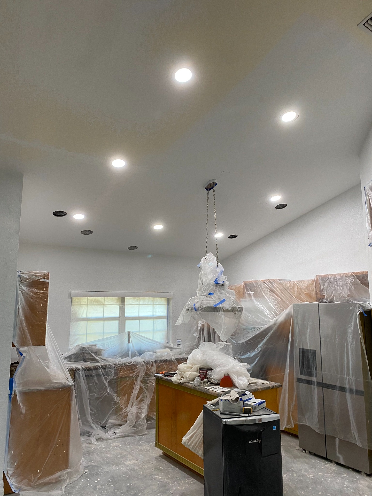 Kitchen remodel in progress with newly installed recessed LED downlights switched on and cabinetry covered in protective plastic.