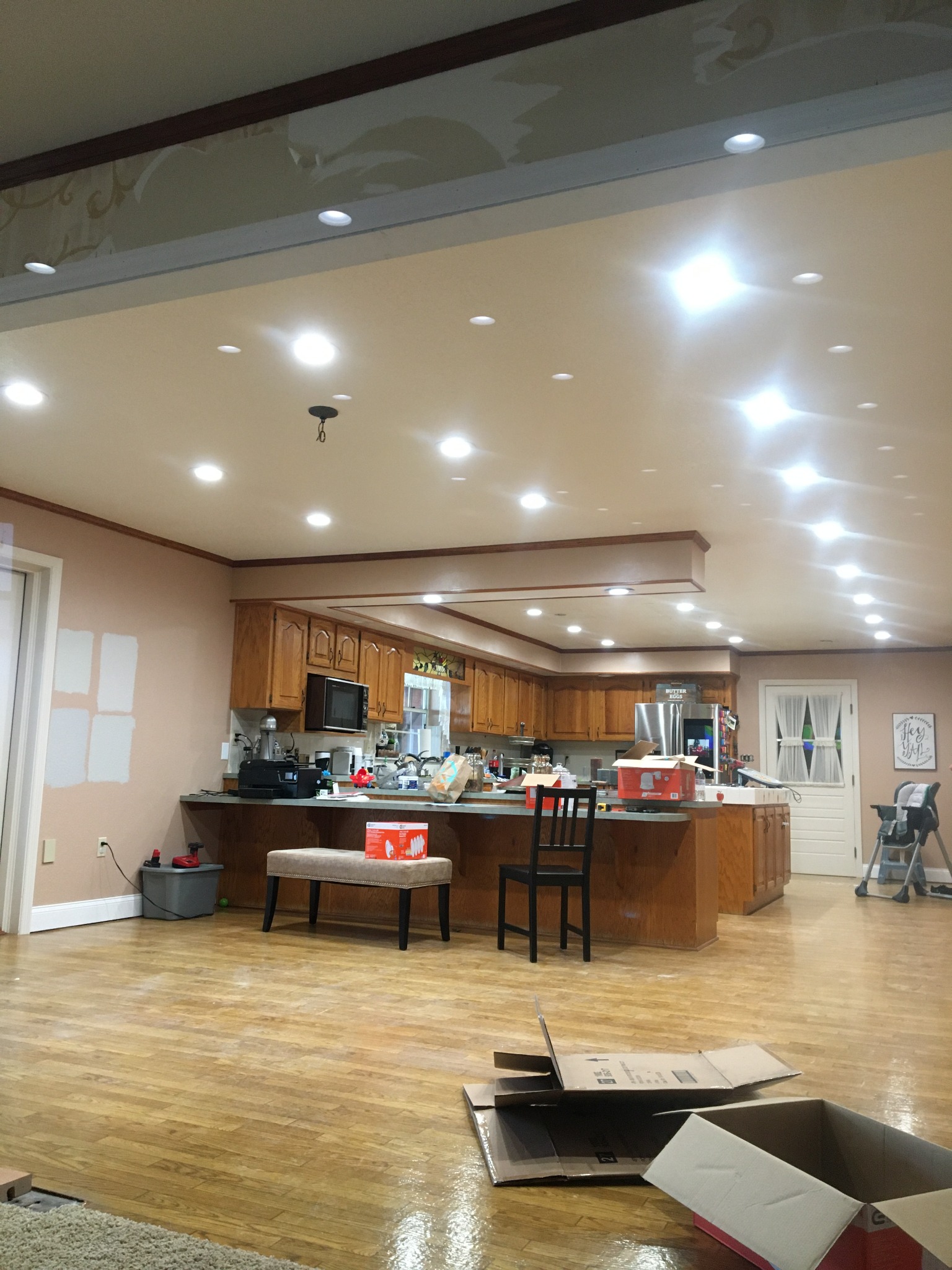 Large open living and kitchen area lit by dozens of warm white recessed LED downlights above hardwood flooring.