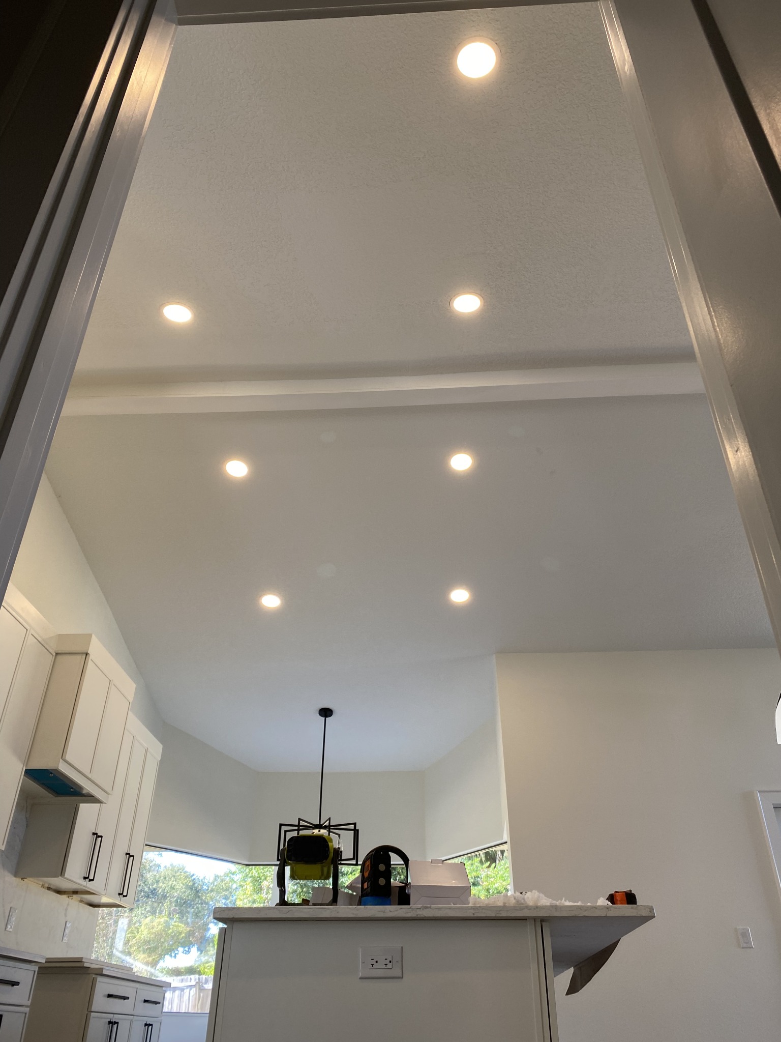 Vaulted kitchen ceiling with an evenly spaced grid of recessed LED downlights above white cabinetry and a lantern pendant over the island.